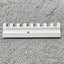 A Silver Reed SK 890 white needle pusher for an electronic knitting machine, placed on a grey surface.