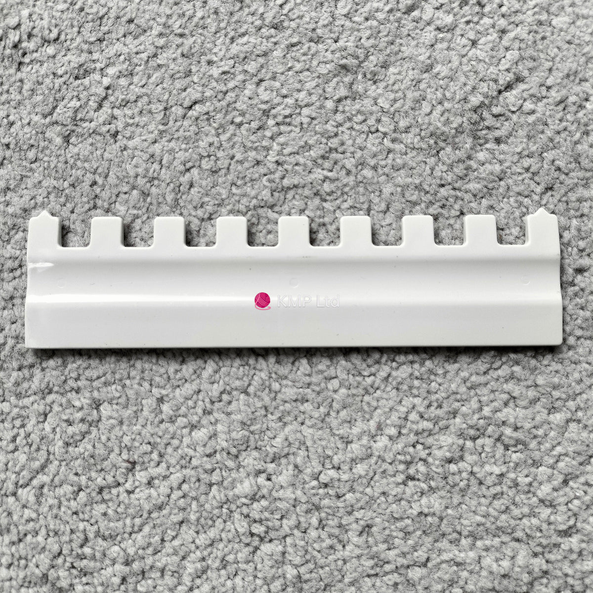 A Silver Reed SK 890 white needle pusher for an electronic knitting machine, placed on a grey surface.