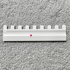 A Silver Reed SK 890 white needle pusher for an electronic knitting machine, placed on a grey surface.