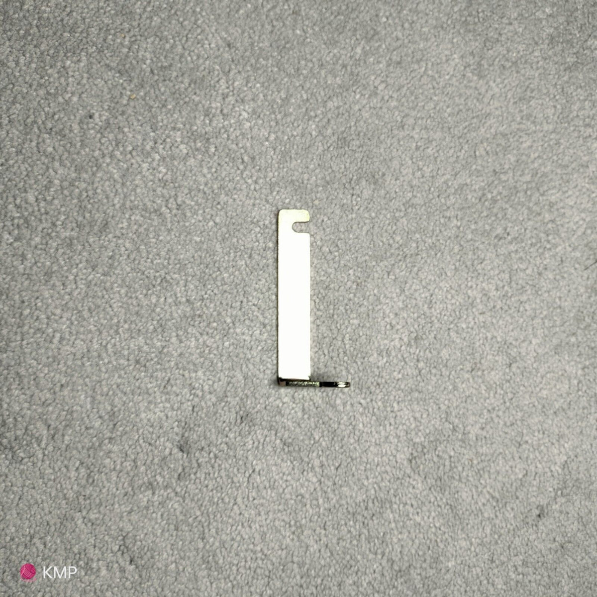 A silver-colored metal lock for a Brother KH-900 Electroknit Knitting Machine, placed on a grey surface.