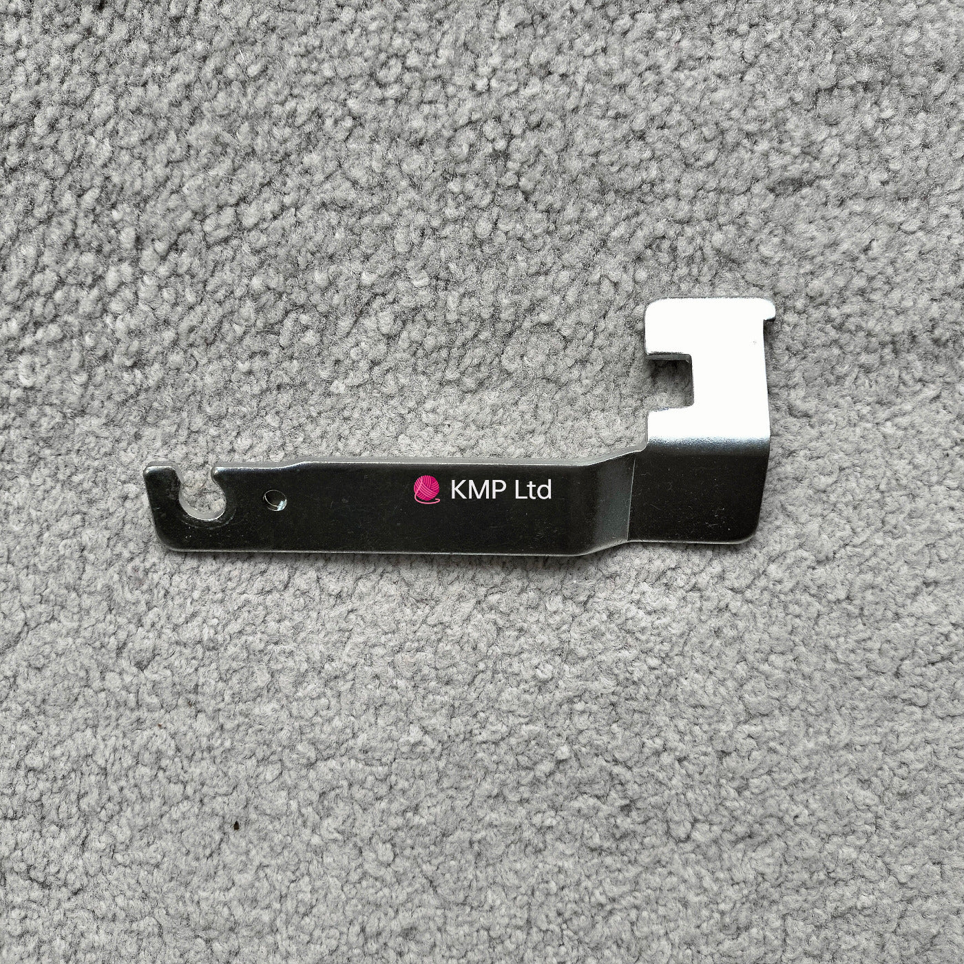 A metal carriage lock for an electronic knitting machine, with a branded name 'Knitting Machine Co Ltd'.
