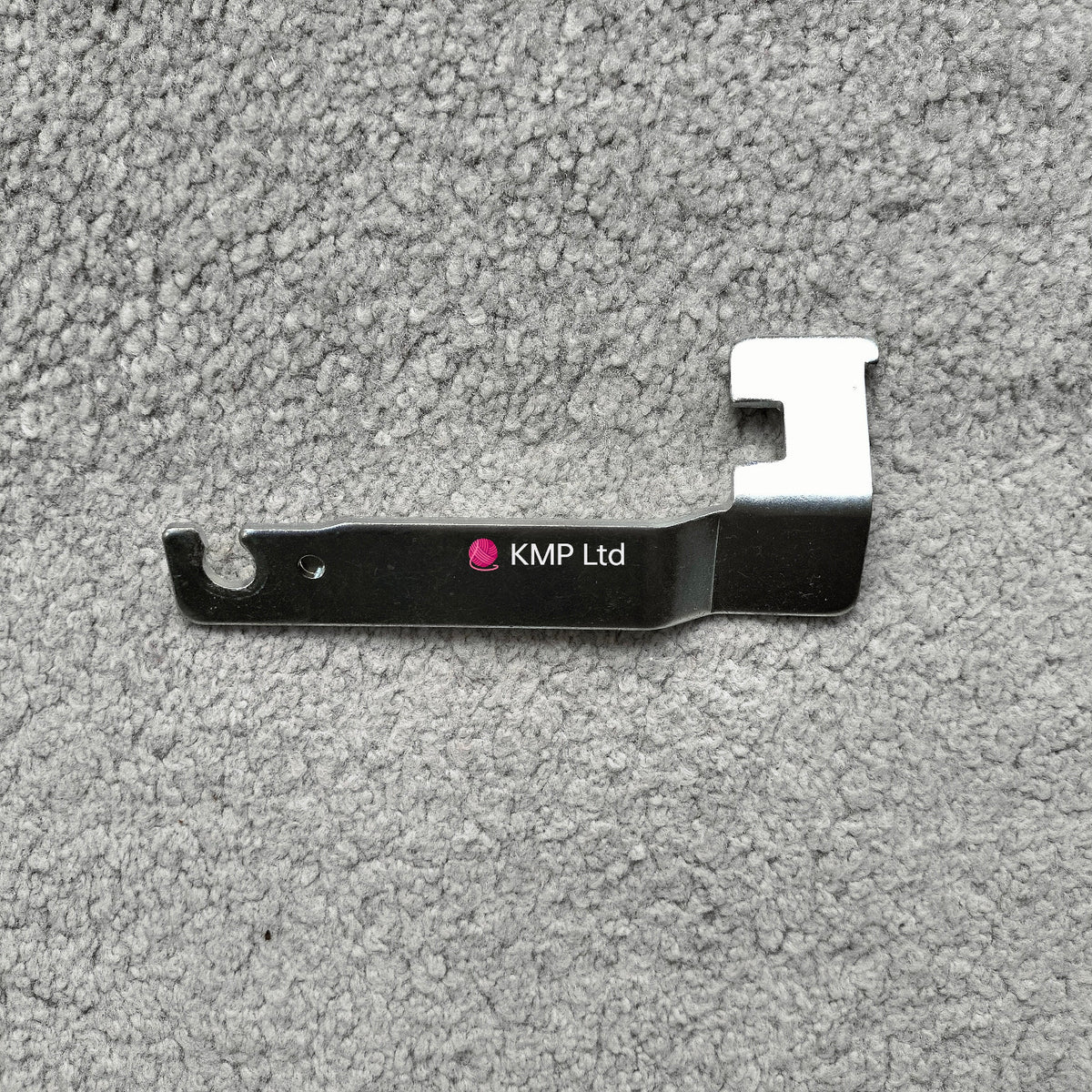 A metal carriage lock for an electronic knitting machine, with a branded name 'Knitting Machine Co Ltd'.